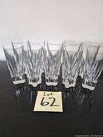 Photo showing a set of ten clear glass tumblers arranged on a dark flat surface.