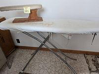 Photo of full-size ironing board with smaller wooden shirt ironing board on top, showing metal legs and light-colored cover with discoloration and wear.
