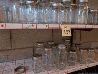Shelves filled with clear glass mason jars with metal lids, assorted sizes, arranged in two rows on metal shelving unit.