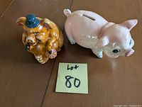 Two ceramic piggy banks side by side on a table: a smooth pink pig and a brown pig with blue hat and pipe