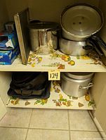 Photo of assorted metal pots and pans arranged on two shelves showing various sizes of pots, pans, baking sheets and trays.