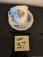 Photo of a Royal Albert bone china cup and saucer with floral pattern and gold trim on a black surface with Lot 37 label visible.
