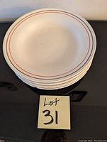 Stack of six white ceramic soup bowls with red double line trim near the rim on top of a dark surface.