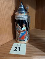 German ceramic drinking stein with a detailed relief of a man and woman sitting at a table, housed in a wooden shelf corner.
