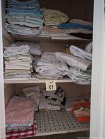 Two shelves showing folded bed sheets on the top shelves and assorted towels on the bottom left and right sides.