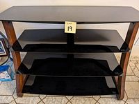 4-tiered glass and wooden shelves TV stand with dark tinted glass shelves and wooden frame, placed on a tiled floor.