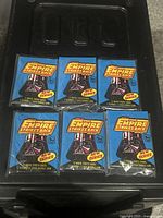 Top view showing six sealed blue wax packs with Darth Vader image and Star Wars branding arranged in two rows of three on a black surface.