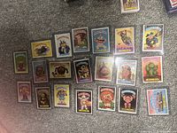 Full lot of 20 Garbage Pail Kids cards laid out on carpet, all in clear plastic protectors showing front artwork and character names.
