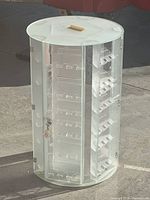 Front and side view of clear acrylic swivel display case with locking door open showing interior shelves and slots for watches or collectibles.