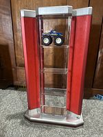 Red and clear acrylic display case with one diecast toy truck placed on second shelf from top. The case shows overall structure and size.