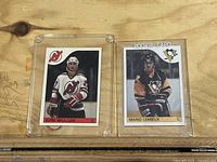 Two O-Pee-Chee hockey cards side-by-side in hard plastic holders; left: Kirk Muller, right: Mario Lemieux rookie.