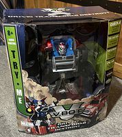 Front view of the Transformer V-Bot RC toy in original packaging. The toy is visible through the box window, showing a robot figure and a red car.
