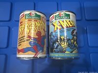 Photo showing two vintage Chef Boyardee coin banks featuring Spider-Man and Wolverine X-Men characters on colorful backgrounds