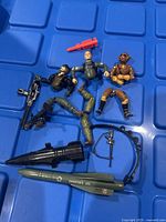 Three partially assembled vintage GI Joe figures and various plastic weapons and accessories including two missiles, rifle, black conical attachment, and black harness with small weapons