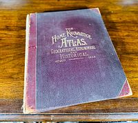 Top view of the large atlas showing aged maroon cover with gold embossed title text about geographical, astronomical and historical content.