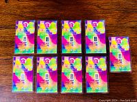 Nine unopened 1 grain .999 fine silver bullion bars in colorful Benchmark Strategic Metals packaging on a wooden surface.