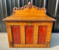 Front view of antique oak wall desk showing carved wooden trim and three inset front panels with darker wood and carved accents.