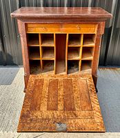 Front view of antique wall desk with fold-down panel open, showing cubbies and drawers, wood grain visible.