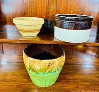 Three antique stoneware items: beige mixing bowl, two-tone crock, and multi-colored planter
