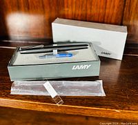 Overview of matte black LAMY fountain pen in original box with blue ink cartridge and outer box.
