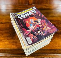 Large stack of Conan the Barbarian comic magazines with color covers on wooden surface.