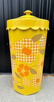 Front view of yellow metal laundry basket with scalloped lid and orange floral design.