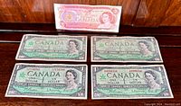 Five Canadian banknotes laid out on a wooden surface showing front side, including four 1967 Centennial one dollar bills and one 1974 two dollar bill