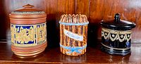 Front view of all three Victorian tobacco jars on wooden shelf, showing details and different styles