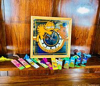 Framed Garfield mirror clock and 12 Garfield bookmarks arranged on a wood shelf