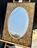 Full view of the vintage oval mirror standing on a bamboo stand showing detailed embossed gilded floral wood frame.