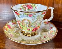 Teacup and saucer front view showing garden scene and rose border on cup and saucer with gold trim