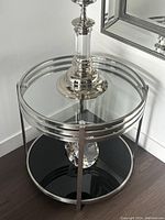 Table shown from an overhead angle with decorative lamp and mirror in background, highlighting clear glass top and chrome band detailing.