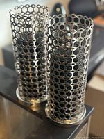 Pair of cylindrical chrome candle holders with open honeycomb lattice design on a table.