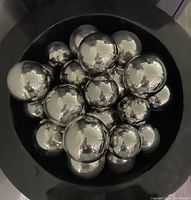 Top view of 36 reflective silver balls of various sizes, footed, clustered inside a large black bowl/container.
