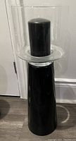 Pair of black glass turret candle holders photographed against a wall, each with a clear glass cylindrical top holding a black pillar candle. The holders have a glossy finish and are approximately 60cm tall.