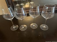 Four clear glass red wine goblets standing upright on a dark surface with reflection visible in a mirror behind them.