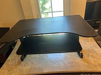 Image of black adjustable sit-to-stand desk converter on marble countertop, showing large upper desk surface and lower sliding keyboard tray.