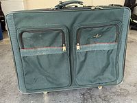 Front view of Atlantic black suitcase with two zippered pockets and handle on top, showing fabric texture and wear marks.