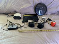 Full lot laid out on bed including clock radio, keyboard, mice, portable speakers, and cables
