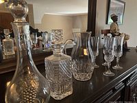 Row of crystal drinkware including decanters and glasses on a dark wooden surface with mirror background