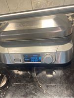 Front view of closed Cuisinart GR-5B grill showing stainless steel body, digital display, control knob and power button.