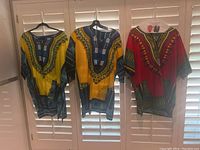 Three African dashiki shirts hanging on hangers, showing front colorful patterns and design