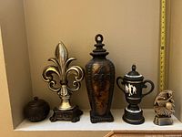Front angle photo of the five decorative statues and trophies arranged on a shelf showing details and scale with measuring tape.