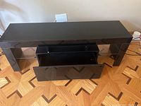 Front view of black entertainment center with large open drawer and shelf in the middle.