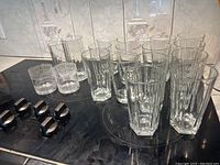 Fourteen large clear ribbed 16 ounce glasses grouped with four smaller ribbed clear glasses on a table.