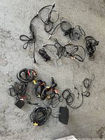 Lot of assorted cables on concrete floor, including HDMI, USB, and composite AV cables.
