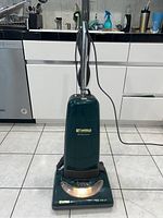 Full view of upright Kenmore vacuum cleaner, dark green, showing handle and base on tile floor.