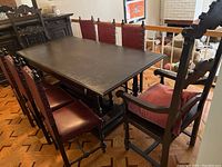 View of a dining table surrounded by six chairs including four leather-upholstered wooden chairs and two larger wooden end chairs with cushions.