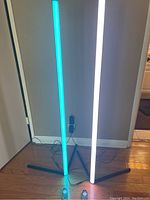 Two modern LED corner floor lamps lit up in blue and white colors with visible remote controls on floor.