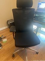 Front view of black office chair showing mesh backrest, padded seat, headrest, and armrests.